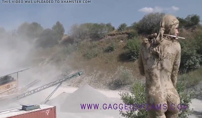 Ball-gagged blonde covered in mud posing outdoors
