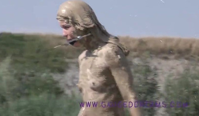 Ball-gagged blonde covered in mud posing outdoors