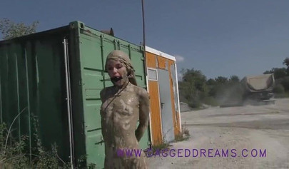 Ball-gagged blonde covered in mud posing outdoors