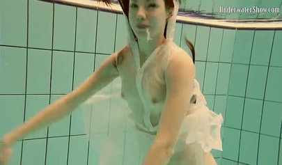 Beautiful teen swimming in the pool in her white sheer dress